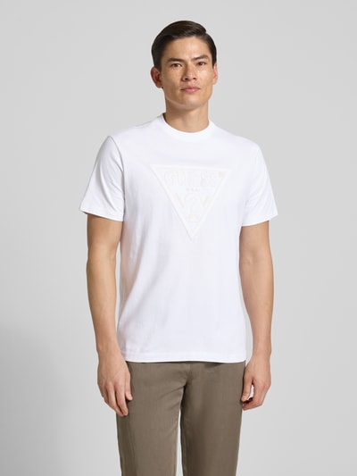 Mannenmodel draagt T-Shirt met Logo en Rundhalsausschnitt van Guess, witte katoenen regular fit met logoprint, ruglengte maat M 70 cm, volledig zicht van voren