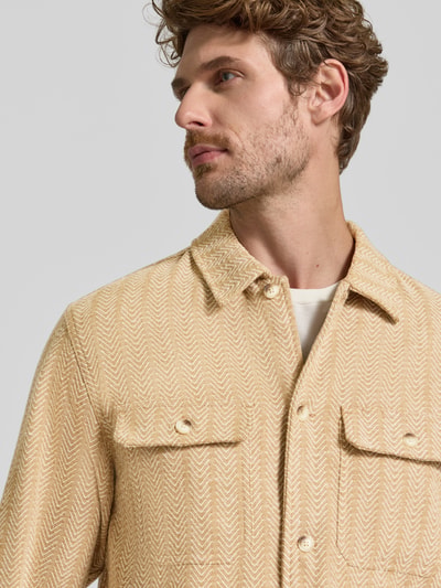 Männermodel trägt Relaxed Fit Hemdjacke mit Brusttaschen von Scotch & Soda, hellbeige Zickzack-Muster, Knopfleiste, Nahaufnahme Oberkörper.