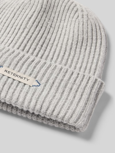 Produktfoto, hellgraue Mütze in Strick-Optik Modell 'L’ATELIER' von RETERNITY, breiter Umschlag, Label-Patch sichtbar, weiche Textur.