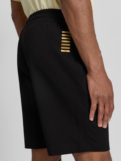 Männermodel trägt Shorts mit elastischem Bund und Logo von EA7 Emporio Armani aus reiner Baumwolle, Regular-Fit, Detailaufnahme Rückansicht.
