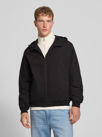 Männermodel trägt Regular Fit Jacke mit Kapuze Modell 'Charge' von JACK & JONES in Schwarz, glatte Textur, Reißverschluss, Ganzkörperansicht von vorne. Damen Jacke, Rückenlänge 68 cm, Schulterbreite 50 cm, Brustweite 60 cm, Ärmellänge 66 cm.
