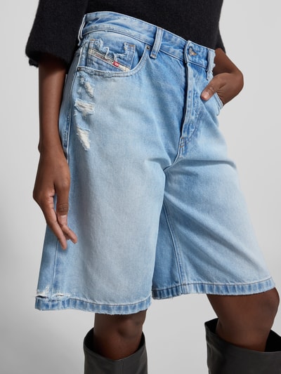 Frauenmodel trägt Relaxed Fit Jeansshorts aus Baumwolle von Diesel in hellem Blau mit Destroyed-Look und 5-Pocket-Design, Nahaufnahme Oberkörper.