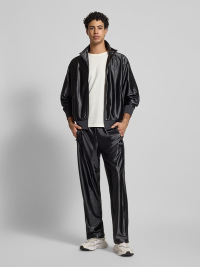 Męski model nosi spodnie treningowe z logo, model 'FIREBIRD' od adidas Originals, krój regular fit, elastyczny pas, długość wewnętrzna 79 cm, widok całej sylwetki z przodu.