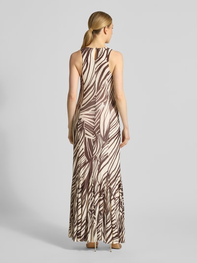 Frauenmodel trägt Maxikleid mit rückseitigem Schlüsselloch-Ausschnitt von Guess, braun-beiges Blättermuster, Rundhalsausschnitt, Ganzkörperansicht Rückansicht. Material-Mix mit Stretch-Anteil, körpernaher Schnitt, blickdichtes Unterkleid, breite Träger, Länge bei Größe S etwa 139 cm.