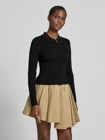 Frauenmodel trägt Slim Fit Jacke aus Viskose-Mix von Victoria Beckham in Schwarz mit Polokragen, Strick-Optik und Reißverschluss, Ganzkörperansicht von vorne.