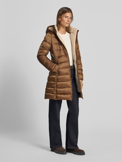 Frauenmodel trägt Steppmantel mit abnehmbarer Kapuze Modell 'CLELIA' von Save The Duck in Braun, glatte und gesteppte Textur, Ganzkörperansicht von vorne.
