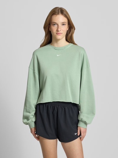 Frauenmodel trägt Relaxed Fit Pullover mit Logo-Stitching Modell 'Chill' von Nike aus grünem Baumwoll-Mix mit Rundhalsausschnitt und elastischen Ärmelabschlüssen, Ganzkörperansicht von vorne.