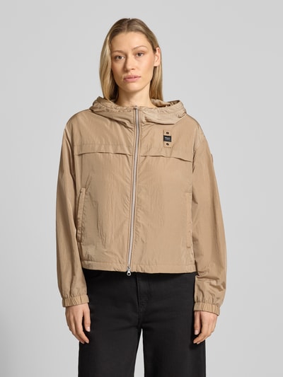 Frauenmodel trägt Trekking Jacke mit Kapuze Modell 'BURRAGE' von Blauer Usa in Beige, zweiwege-Reißverschluss, gerade geschnitten, Label-Patch, seitliche Reißverschlusstaschen, elastische Ärmelabschlüsse, glatte Textur, Ganzkörperansicht von vorne