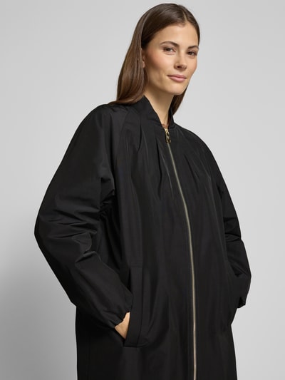 Frauenmodel trägt Mantel mit Stehkragen und Zweiwege-Reißverschluss von Fuchs Schmitt in Schwarz, aus Material-Mix mit Baumwoll-Anteil, Relaxed Fit, Eingrifftaschen, Nahaufnahme Oberkörper.
