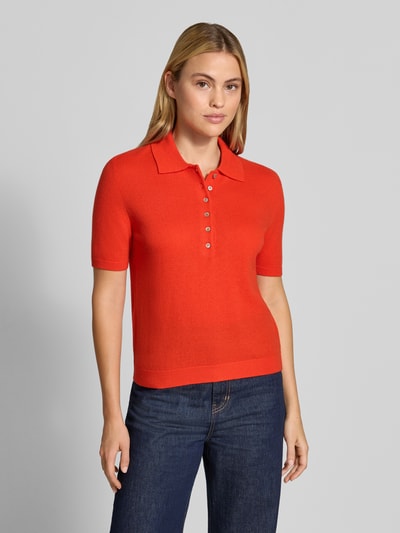 Frauenmodel trägt Poloshirt aus reiner Wolle von Stefanel in leuchtendem Rot, taillierte Passform, Polokragen, gerippte Abschlüsse, Ganzkörperansicht von vorne.