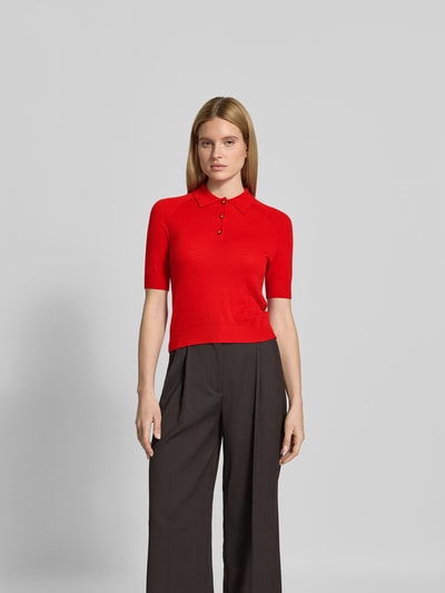 Frauenmodel trägt Poloshirt aus reiner Wolle von Victoria Beckham in Rot, Strick-Optik, Halbarm, Regular Fit, Ganzkörperansicht von vorne.