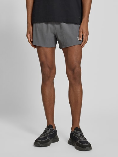 Männermodel trägt Relaxed Fit Shorts mit integriertem Slip von EA7 Emporio Armani, Elastischer-Material-Mix, Strukturmuster, Logo-Patch, Bund, Ganzkörperansicht von vorne.