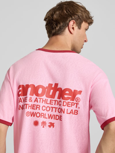 Männermodel trägt T-Shirt mit Label-Print und Rundhalsausschnitt von ANOTHER COTTON LAB in Rosa mit rotem Print, Reine Baumwolle, Relaxed-Fit, Rückenlänge 62 cm bei Größe M, Ganzkörperansicht Rückansicht