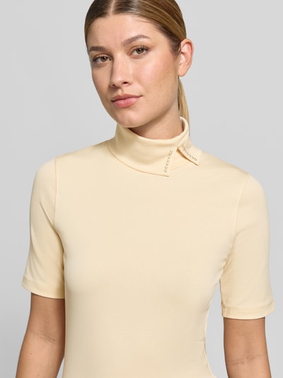 Vrouwenmodel draagt Slim Fit T-shirt uit katoenmix van Marc Clain in licht beige met asymmetrische col en siersteentjes, Nahaufnahme Oberkörper, Ruglengte maat 36: 56 cm.
