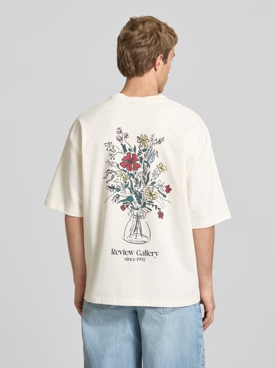 Männermodel trägt T-Shirt mit Stitching und Rundhalsausschnitt von REVIEW in Creme mit farbigem Blumenprint, Oversized, reine Baumwolle, Ganzkörperansicht Rückansicht.
