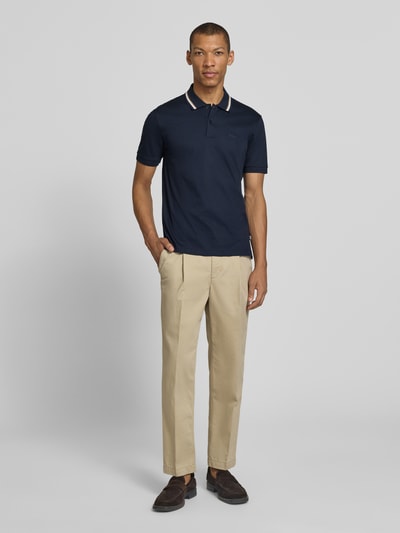 Männermodel trägt Slim Fit Poloshirt aus reiner Baumwolle Modell 'PENROSE' von BOSS in Dunkelblau, kurzarm, unifarben, Ganzkörperansicht von vorne.