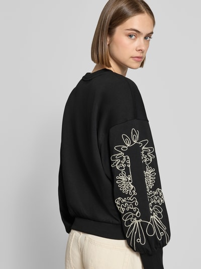 Kobieta nosi Relaxed Fit Sweatshirt aus Baumwoll-Mix model 'BROOKE' od ONLY, czarny z jasnym haftem na rękawie, widok całej sylwetki z tyłu, bluza damska od ONLY
