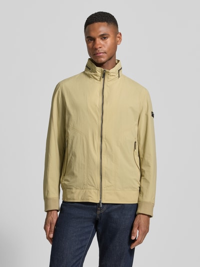Männermodel trägt Regular Fit Jacke mit Stehkragen von bugatti in Beige, Zweiwege-Reißverschluss, strukturierte Oberfläche, Ganzkörperansicht von vorne.