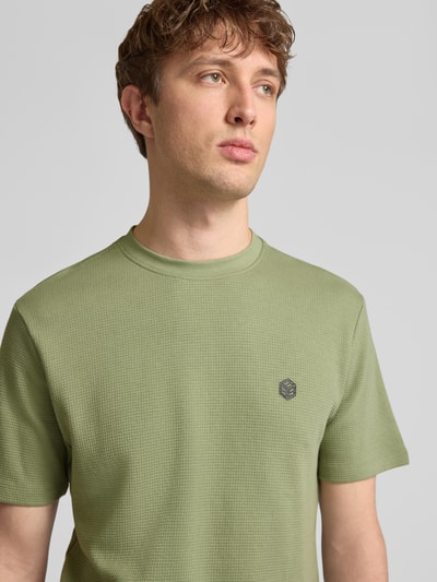 Männermodel trägt T-Shirt mit Label-Detail Modell 'FILLIP' von Blend in Grün, Reine Baumwolle, Gerader-Schnitt, Nahaufnahme Oberkörper.