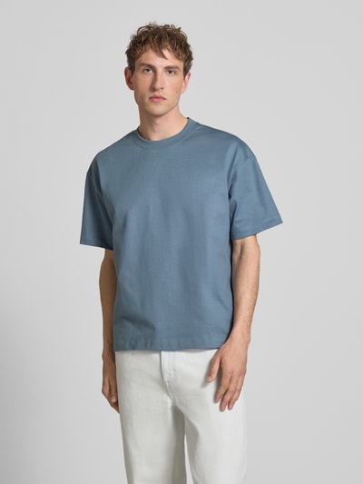 Männermodel trägt Boxy Fit T-Shirt aus reiner Baumwolle von Marc O'Polo Denim, unifarbenes Blau, Rundhals, Label Print, Ganzkörperansicht von vorne.