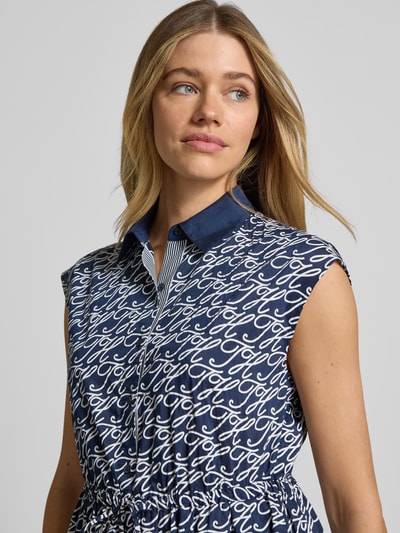 Frauenmodel trägt Hemdblusenkleid in Midi-Länge aus Baumwolle-Seide-Mix von Tommy Hilfiger mit Allover-Muster, tailliert, Ausschnitt mit Hemdblusenkragen, ohne Ärmel, Logo-Print, Taillenband und Knopfleiste, Nahaufnahme Oberkörper.