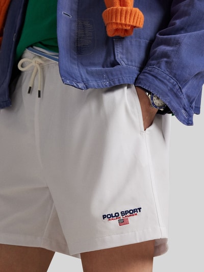 Männermodel trägt weiße Badeshorts mit Label Stitching von Polo Ralph Lauren, unifarben, elastischer Bund, seitliche Taschen, Nahaufnahme Oberschenkel.