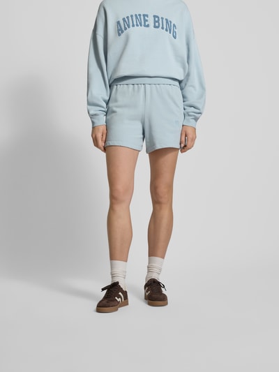 Frauenmodel trägt Regular Fit Shorts mit Logo-Stitching von Anine Bing aus reiner Baumwolle in Hellblau, elastischer Bund, Eingrifftaschen, Ganzkörperansicht von vorne.