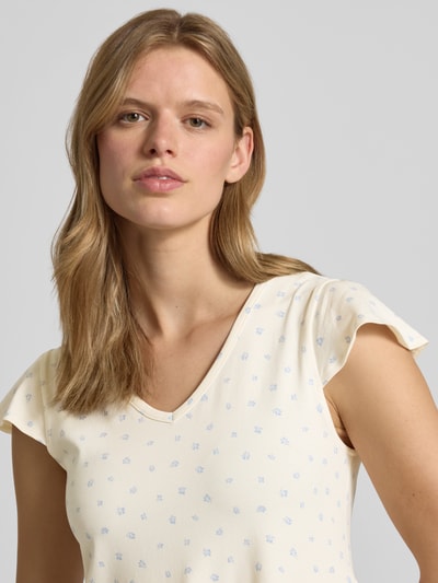 Frauenmodel trägt Minikleid im Stufen-Look mit V-Ausschnitt von REVIEW, cremefarben mit zarten blauen Blümchen, Nahaufnahme Oberkörper. Baumwoll-Elasthan-Mix, A-Linie, Rückenlänge 84 cm, Brustweite 45 cm bei Größe S.