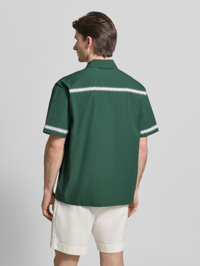 Männermodel trägt Regular Fit Freizeithemd mit aufgesetzten Taschen von WOODBIRD in Dunkelgrün mit weißen Stitchings, ganzkörperansicht Rückansicht. Context: heren vrijetijdshemd van WOODBIRD, regular fit, kentkraag, model 'Wang', stitchings, knoopsluiting, opgestikte zakken, ruglengte bij maat M: 72 cm, schouderbreedte bij maat M: 53 cm, mouwlengte bij maat M: 26 cm.