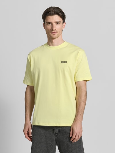 Männermodel trägt T-Shirt mit Label-Print Modell 'Baine' von WOODBIRD aus reiner Baumwolle im Regular-Fit, gelb, Nahaufnahme Oberkörper.