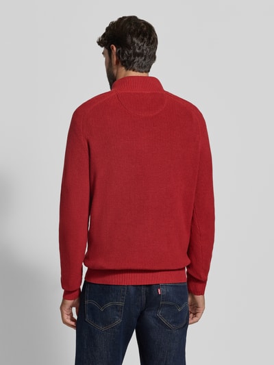Męski model nosi Regular Fit Strickpullover aus reiner Baumwolle mit Troyer-Kragen od Fynch-Hatton w kolorze czerwonym, tekstura dzianiny, mankiety i dół prążkowane, logo haftowane, długi rękaw, krój regular fit, widok całej sylwetki z tyłu