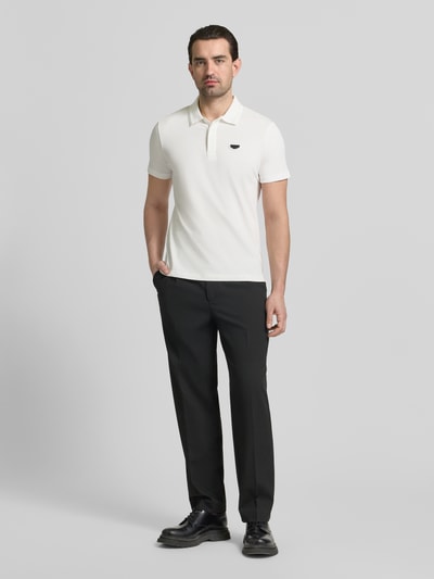 Männermodel trägt Slim Fit Polo-Shirt mit Logo-Applikation von Antony Morato in Weiß zu schwarzer Hose, reine Baumwolle, Ganzkörperansicht von vorne.