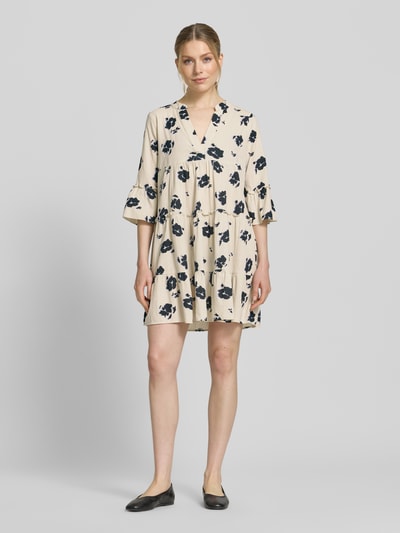 Frauenmodel trägt Ausgestelltes Blusenkleid aus reiner Baumwolle Modell 'DICTHE' von Vero Moda, Optik:Allover-Muster, Mini-Länge, Raffung, Henley-Ausschnitt, 1/2-Arm, Trompetenärmel, helle Grundfarbe mit dunklem Muster, leichte Textur, Ganzkörperansicht von vorne.