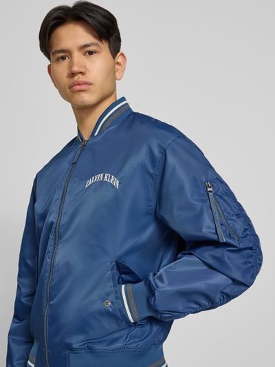 Mannenmodel draagt Regular Fit College-jack met Label Stitching van Calvin Klein Jeans in look: effen, applicatie met labelstitching, contraststrepen, lange mouw, collegekraag, ritssluiting, klepzakken, rompzoom en mouwboord: geribd. Nahaufnahme bovenlichaam.
