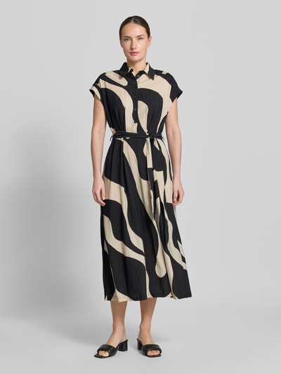 Frauenmodel trägt Hemdblusenkleid mit Bindegürtel Modell 'NIKITA' von Mango, Viskose-Mix, Taillierter Schnitt, Midikleid, abstraktes creme-schwarzes Muster, Hemdblusenkragen, Knopfleiste, Ärmel mit fixiertem Aufschlag, Ganzkörperansicht von vorne.