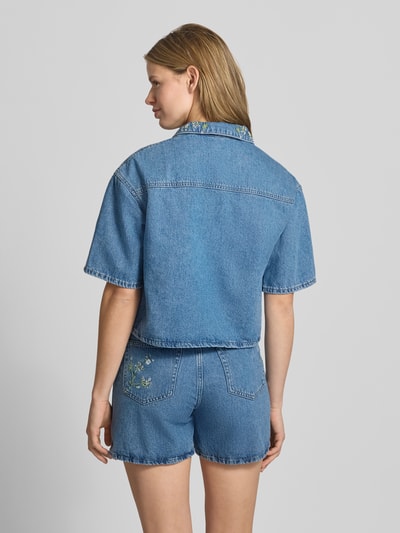 Frauenmodel trägt Boxy Fit Jeansbluse aus reiner Baumwolle Modell 'SKY' von Pieces in Denim-Optik mit Hemdblusenkragen, Stickerei, Rückenpasse, einreihiger Knopfleiste, Kurzarm, Brusttasche, Ganzkörperansicht Rückansicht.