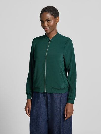 Frauenmodel trägt Regular Fit Blouson mit Reißverschluss-Detail von VERO MODA in Dunkelgrün, glatte Textur, Ganzkörperansicht von vorne.