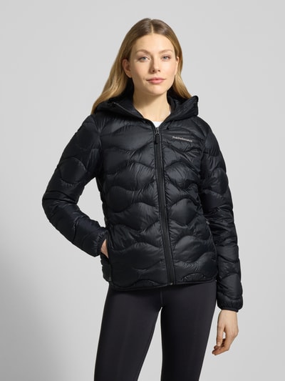 Frauenmodel trägt schwarze Steppjacke mit Daunen-Federn-Füllung Modell 'Helium' von PEAK PERFORMANCE, glatte Textur, Ganzkörperansicht von vorne, Regular Fit, Kapuze, Reißverschluss, Label-Stitching, Länge bei Größe S: 62 cm, Schulterbreite 42 cm, Brustweite 50 cm, Ärmellänge 63 cm.