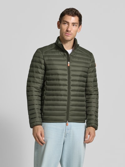 Männermodel trägt olivgrüne Steppjacke mit Zweiwege-Reißverschluss Modell 'ALEXANDER' von Save The Duck, Struktur mit horizontalen Nähten, Stehkragen, Reißverschlusstaschen, Slim Fit, Ganzkörperansicht von vorne.