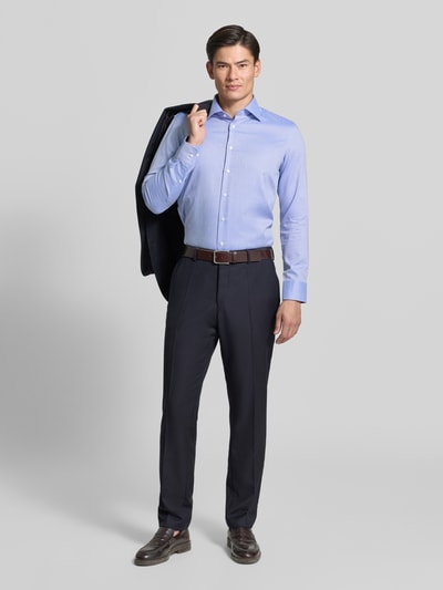 Männermodel trägt Slim Fit Businesshemd aus reiner Baumwolle von Seidensticker in Hellblau, dunkle Hose, neutrale Kulisse, Ganzkörperansicht von vorne.