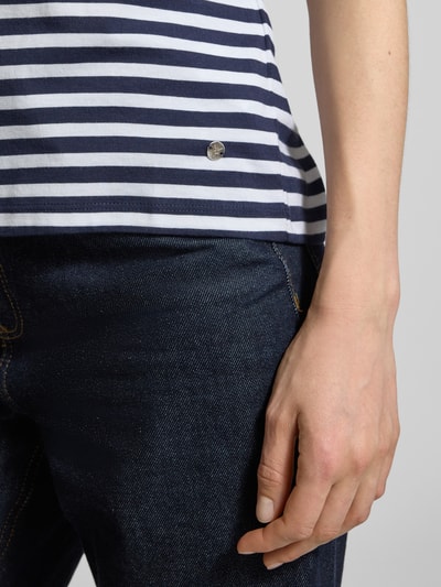 Frauenmodel trägt T-Shirt mit Rundhalsausschnitt und Brusttasche von monari in Weiß-Blau, Streifenmuster, reine Baumwolle, Nahaufnahme Oberkörper.
