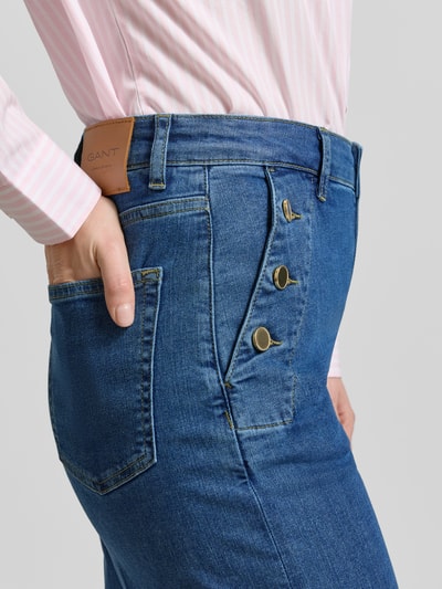 Kobieta nosi Jeans mit seitlichen Knöpfen und Gesäßtaschen od Gant, mieszanka bawełny z dodatkiem streczu, krój regular fit, niebieski denim, zapięcie na boczne guziki, kieszenie z tyłu, detaliczne zdjęcie boczne okolicy biodra.