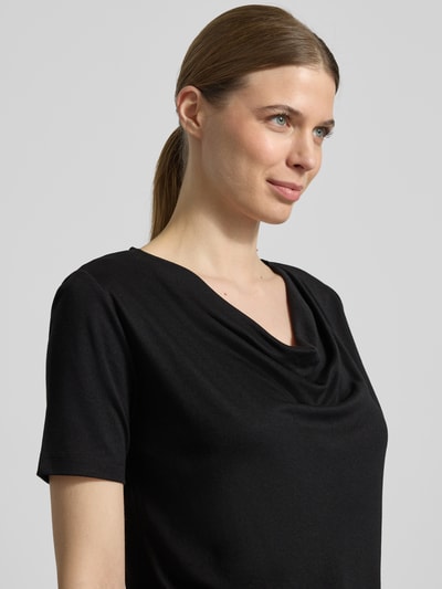 Modelka kobieca ma na sobie T-Shirt mit Wasserfall-Ausschnitt von More & More z czarnego, gładkiego materiału, krój regular fit, długość pleców w rozmiarze 36: 56 cm, zbliżenie na górną część ciała.