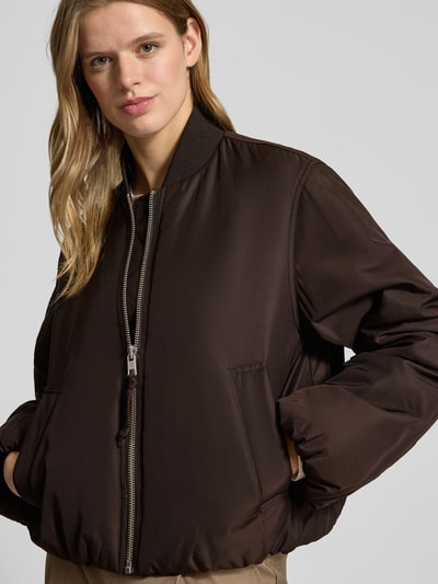 Kobiece modelka nosi Regular Fit Bomberjacke mit College-Kragen von Marc O'Polo Denim, efekt: jednolity kolor, brązowa tkanina, długi rękaw, wyhaftowane logo, zamek błyskawiczny, elastyczne wykończenia, kieszeń wewnętrzna, wpuszczane kieszenie, widok: z przodu, ujęcie górnej części ciała.