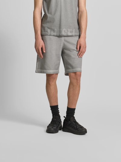 Männermodel trägt Sweatshorts aus reiner Baumwolle von Diesel in Grau mit Used-Look, Label-Print, lockere Passform; Ganzkörperansicht von vorne.