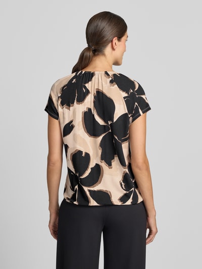 Frauenmodel trägt Regular Fit Kurzarmbluse aus Viskose-Mix Modell 'NOS JULI' von Betty Barclay mit beigem Grundton und schwarzen floralen Mustern, Damen Kurzarmbluse von Betty Barclay, Ganzkörperansicht Rückansicht.