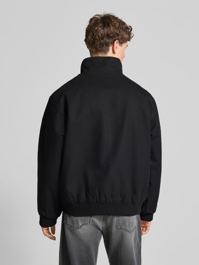 Männermodel trägt Jacke mit Zweiwege-Reißverschluss Modell 'Ravon' von Carhartt Work In Progress aus schwarzer Baumwolle, Rückenansicht, Ganzkörperansicht Rückansicht. Regular Fit, Stehkragen, breite Schultern, schlichte Struktur, dezentes Label-Stitching.