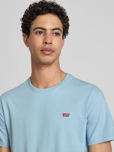 Męski model nosi Regular Fit T-Shirt aus reiner Baumwolle od Levi's®, jednolity, krój regular fit, krótki rękaw, bawełna, z label-aplikacją, jasnoniebieski kolor, zbliżenie na górną część ciała.