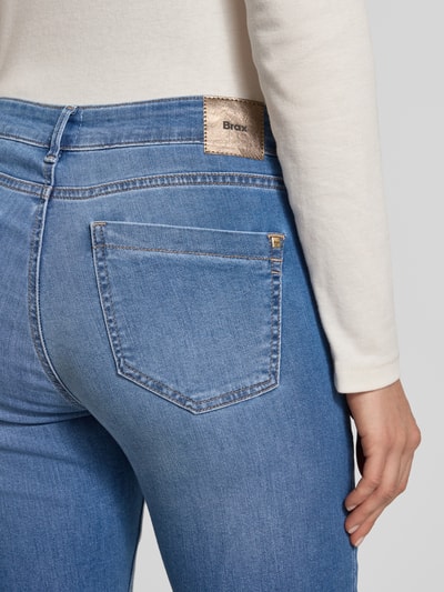 Kobieta nosi Skinny Fit Jeans z kieszeniami model 'SHAKIRA' od Brax, jasnoniebieski denim, używany wygląd, widok z tyłu, zbliżenie na biodra.