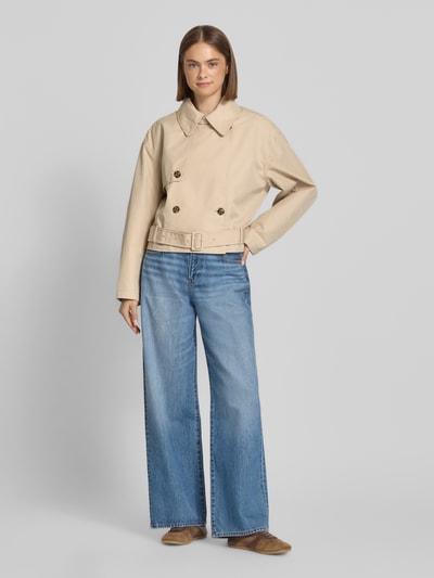 Kobiece modelka nosi Relaxed Fit Trenchcoat aus Baumwoll-Mix od Tommy Jeans, efekt: jednolity kolor, krój relaxed fit, wykładany kołnierz, listwa guzikowa 2-rzędowa, pasek w talii z klamrą z bolcem, długość: krój krótki, naszywka z logo, rękawy: długi rękaw, kieszeń wewnętrzna, wykończenie materiału: splot twill, materiał: mieszanka bawełny, Ganzkörperansicht von vorne.
